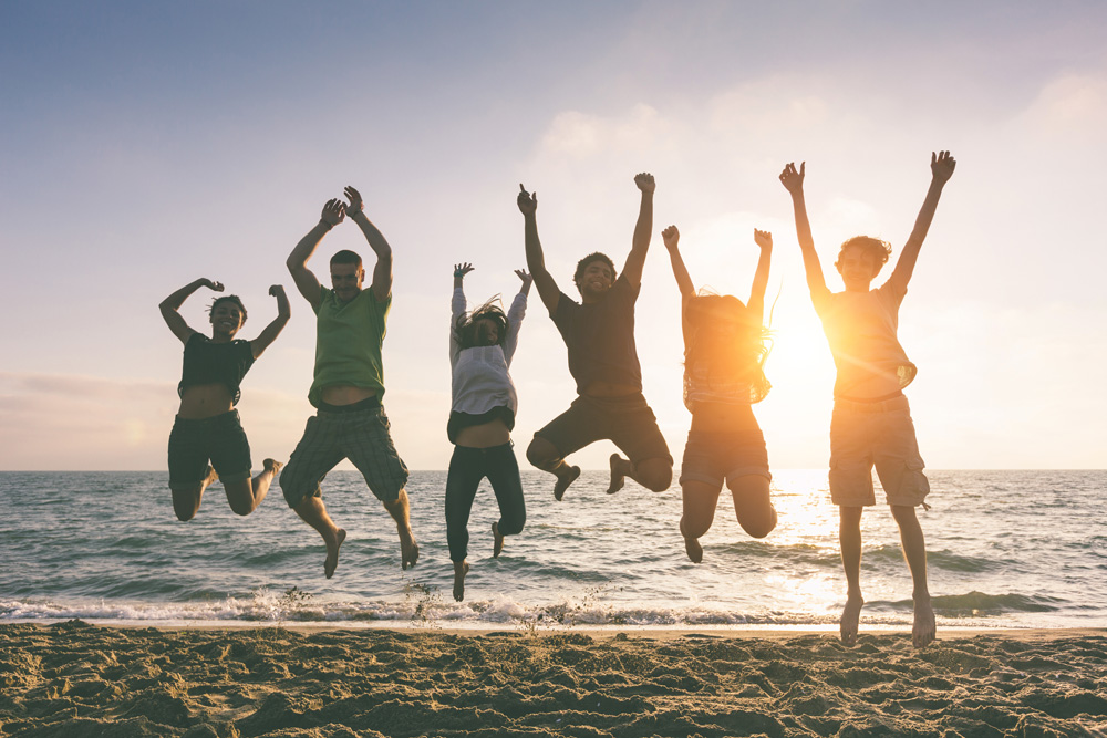Group of 6 people at the beach jumping mid air with the sunset and ocean behind them